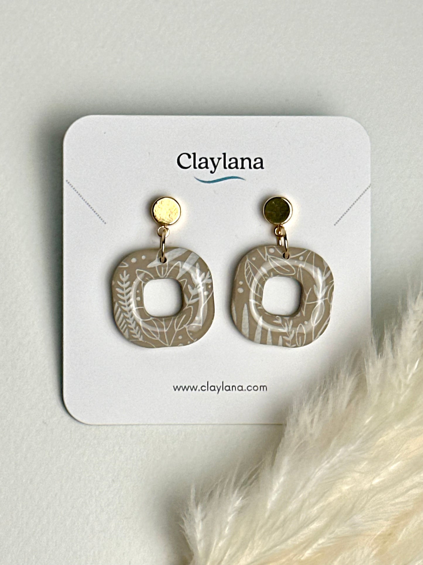 Warm ash brown polymer clay earring with rounded edges and a hollow center, decorated with delicate white autumn leaves on a gold-plated post — a thoughtful, nature-inspired piece to remind you to sparkle with grace.