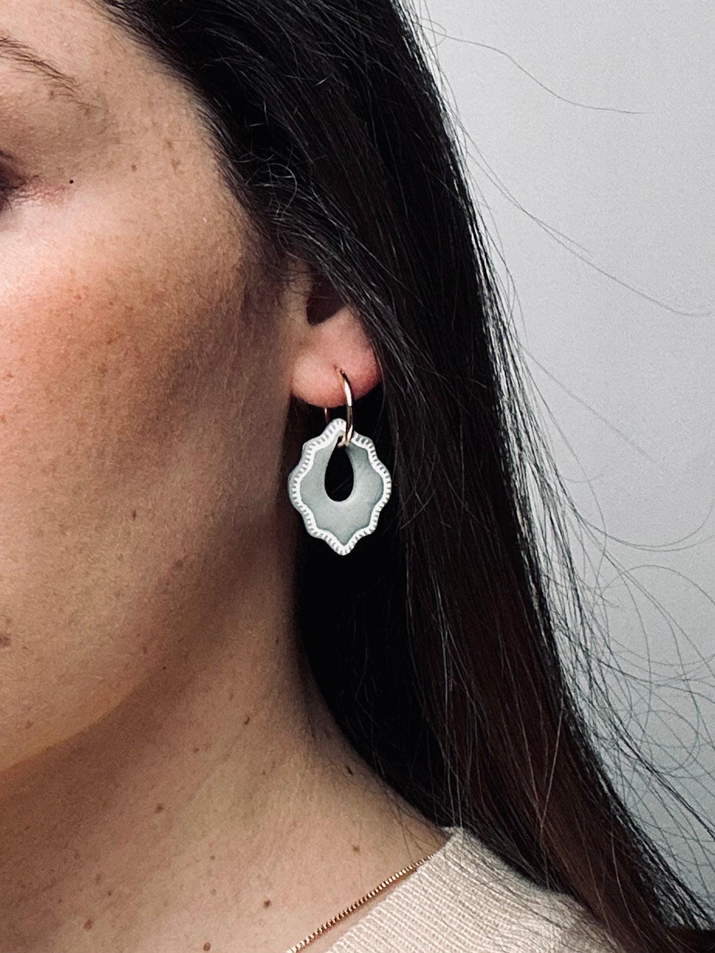 Model wearing Claylana Versilana charms on gold thin earrings.