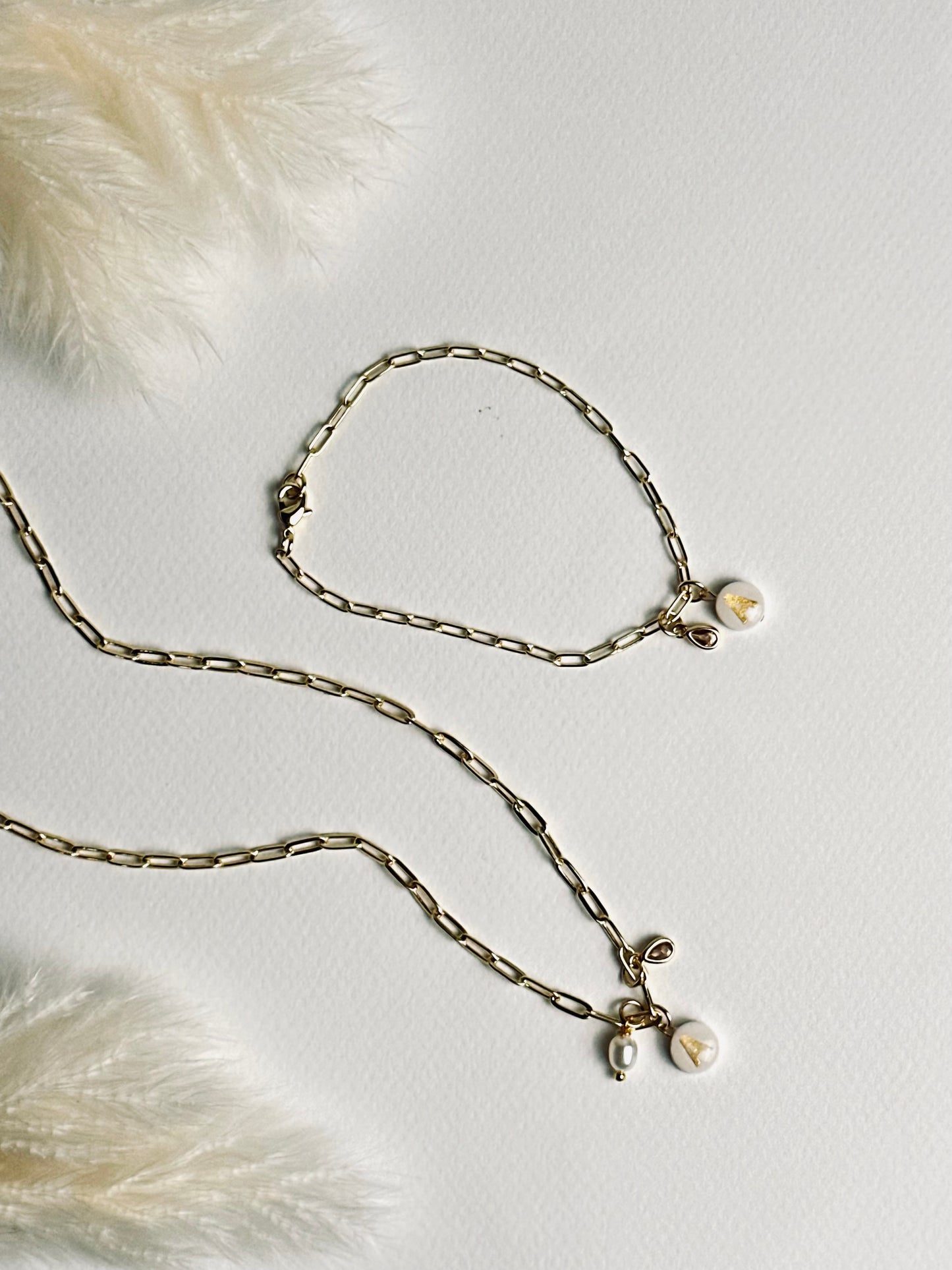 Set from the “Your Story with Grace” collection featuring a personalized clay initial necklace and matching bracelet. Each piece has a white round polymer clay base with a gold initial, paired with 24k gold-filled chains and delicate crystal teardrop accents, creating a coordinated look of elegance, individuality, and thoughtful self-expression.