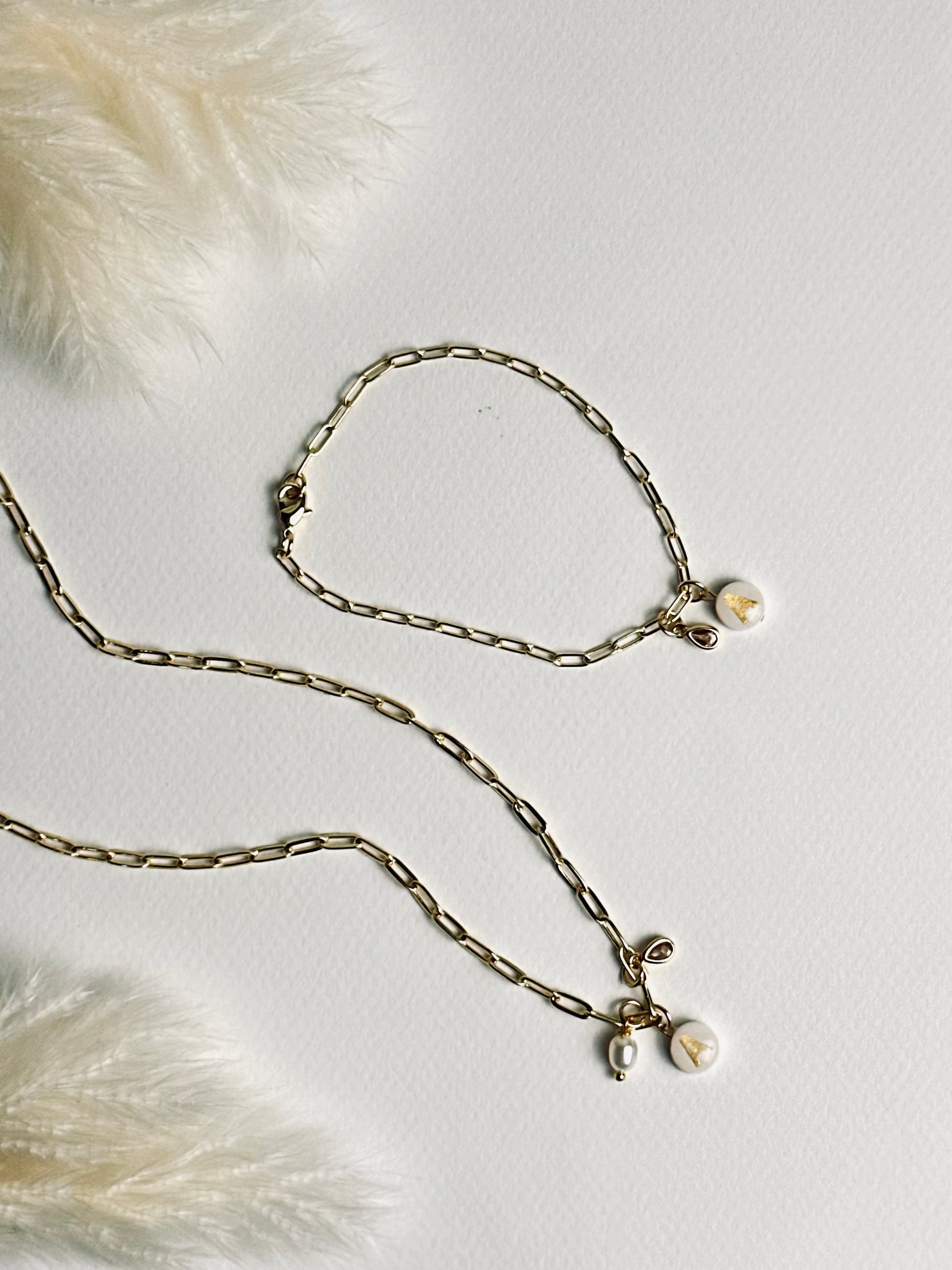 Set from the “Your Story with Grace” collection featuring a personalized clay initial necklace and matching bracelet. Each piece has a white round polymer clay base with a gold initial, paired with 24k gold-filled chains and delicate crystal teardrop accents, creating a coordinated look of elegance, individuality, and thoughtful self-expression.