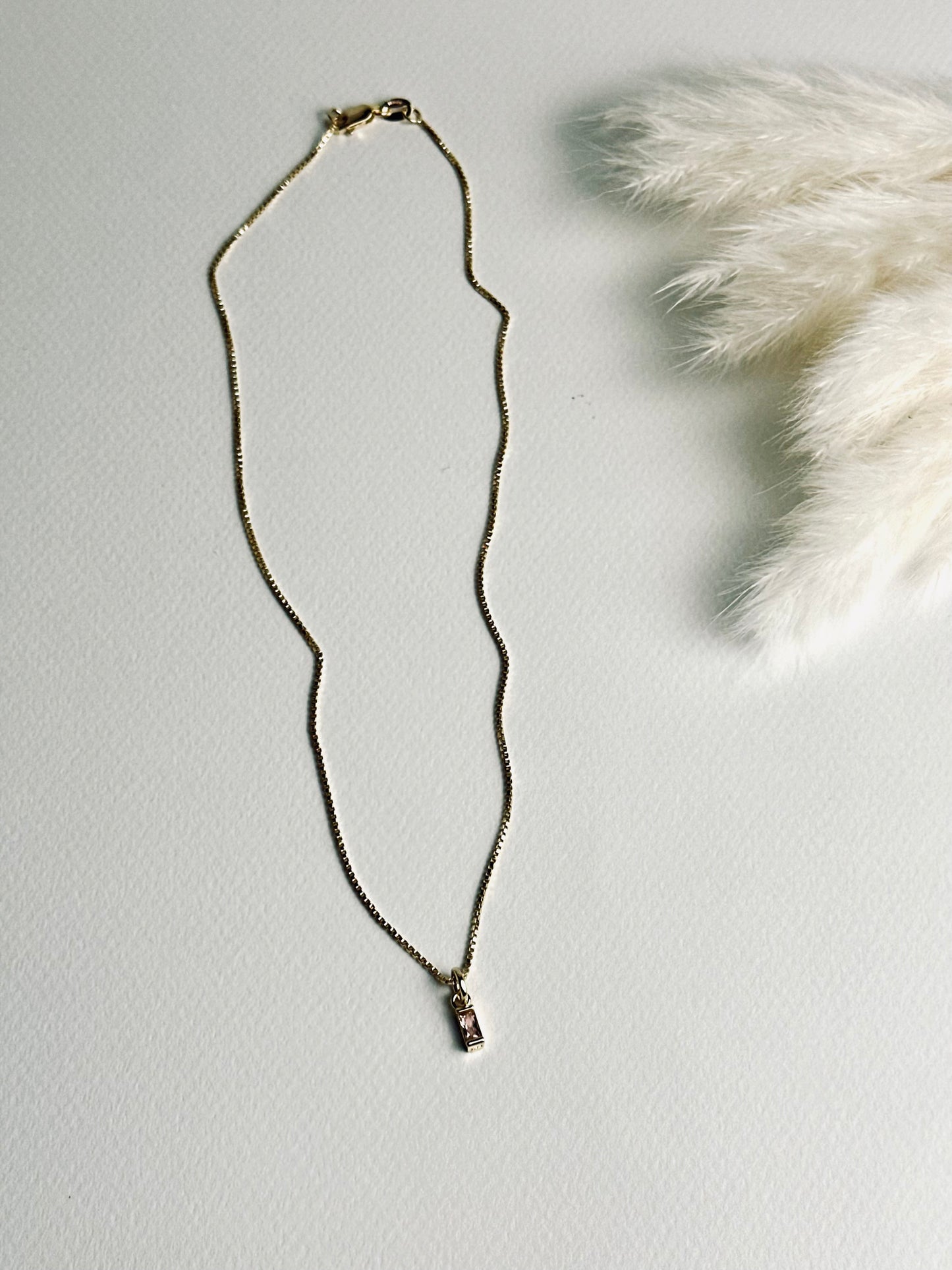 Birthstone necklace laid flat, featuring a single sparkling stone on an 18k gold-filled box chain. The minimalist design captures timeless elegance and personal significance, symbolizing a cherished connection or moment.